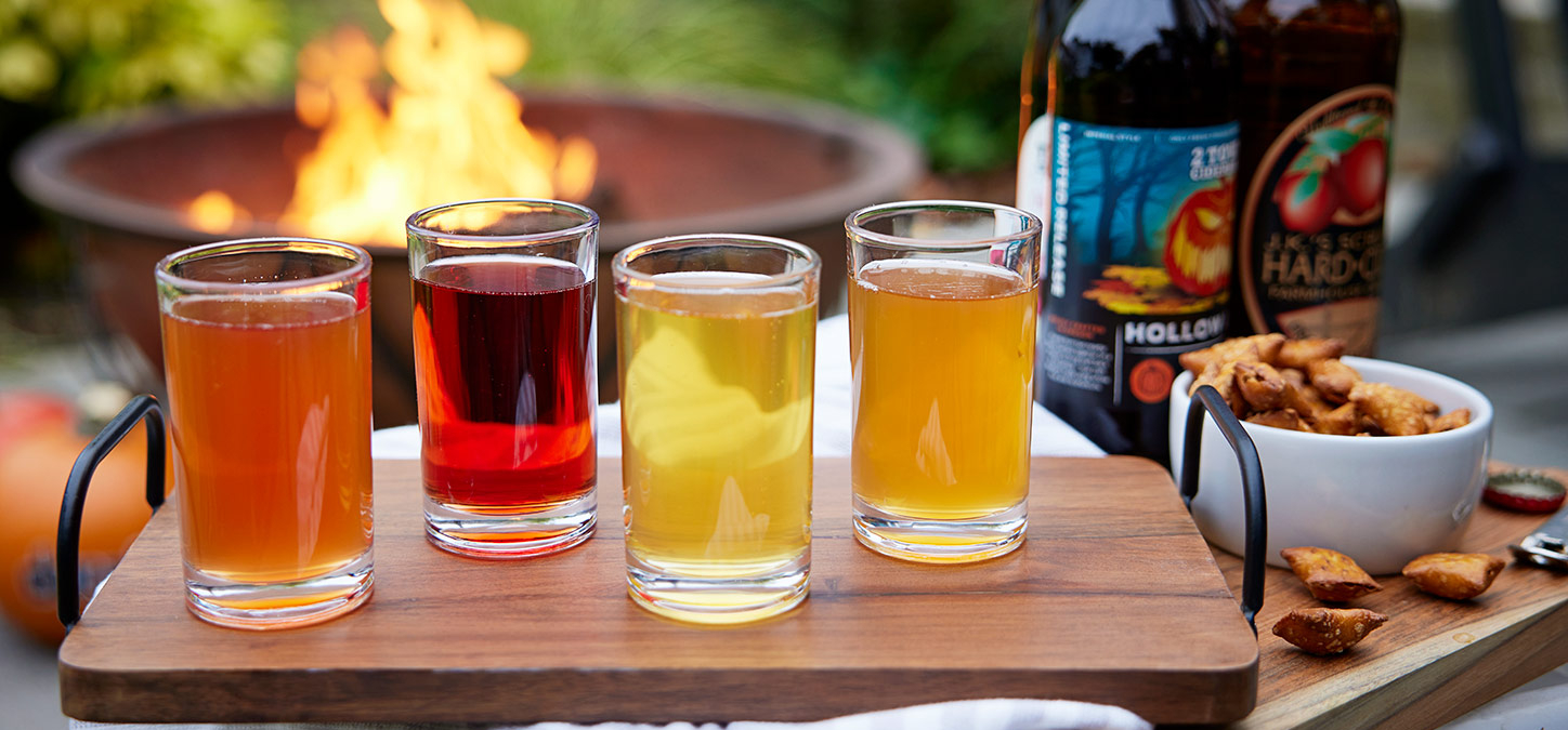 Flight of ciders and snacks with fire pit in background