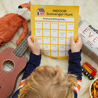 Birds eye view of a guitar, stuffed animal, duraflame firelog, train and child holding Indoor Scavenger Hunt game page