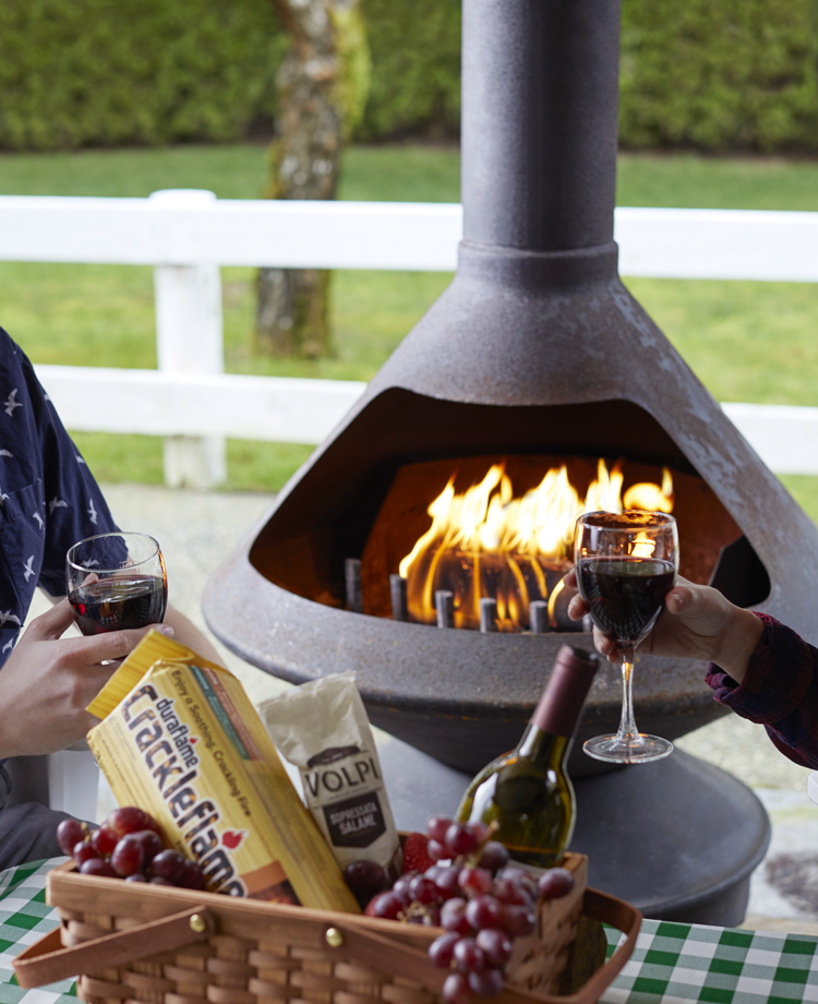 Two people drinking wine together and talking with a Duraflame Crackleflame log burning in an outdoor fireplace in the background