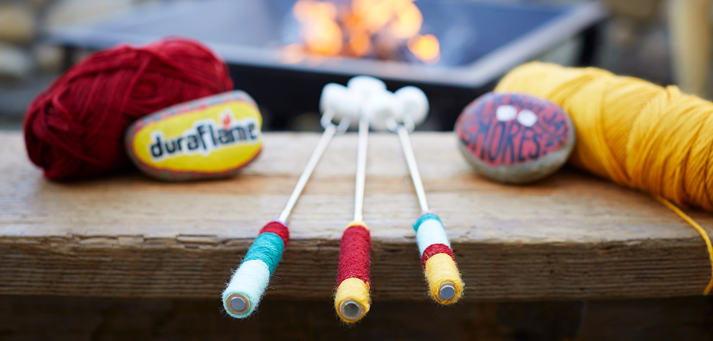 Decorated Roasting Sticks with decorated rocks and balls of yarn with a fire in a fire pit in the foreground