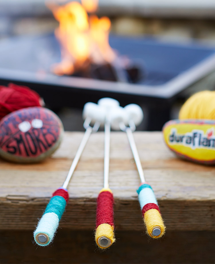 Decorated Roasting Sticks with decorated rocks and balls of yarn with a fire in a fire pit in the foreground