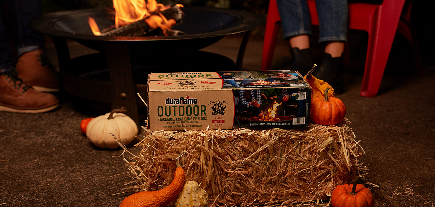 OUTDOOR firelogs package on hay bale with pumpkins and fire pit in the background