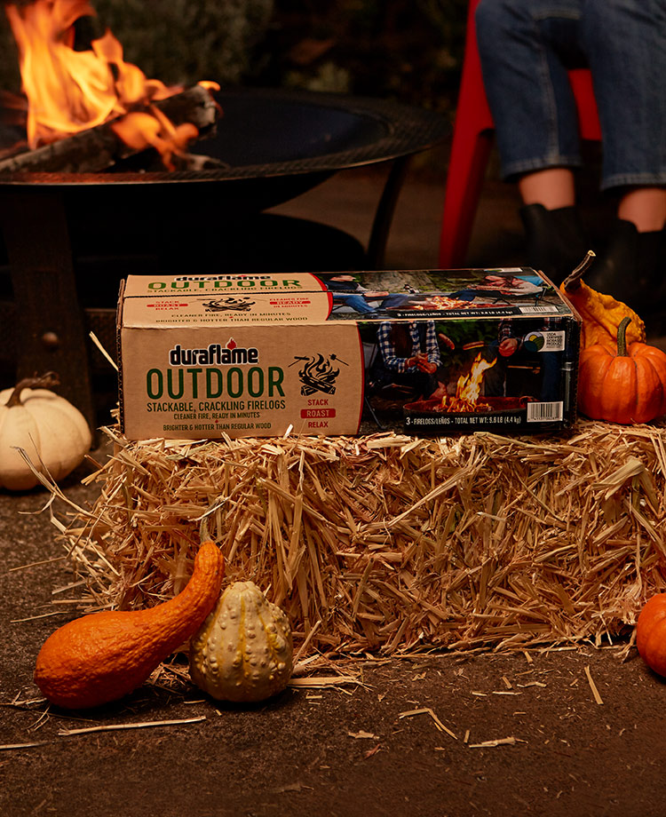 OUTDOOR firelogs package on hay bale with pumpkins and fire pit in the background