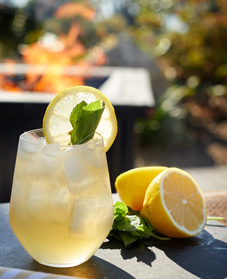 lemonade cocktail with Lemon slice and mint sprig garnish with fire in outdoor fire pit in the background