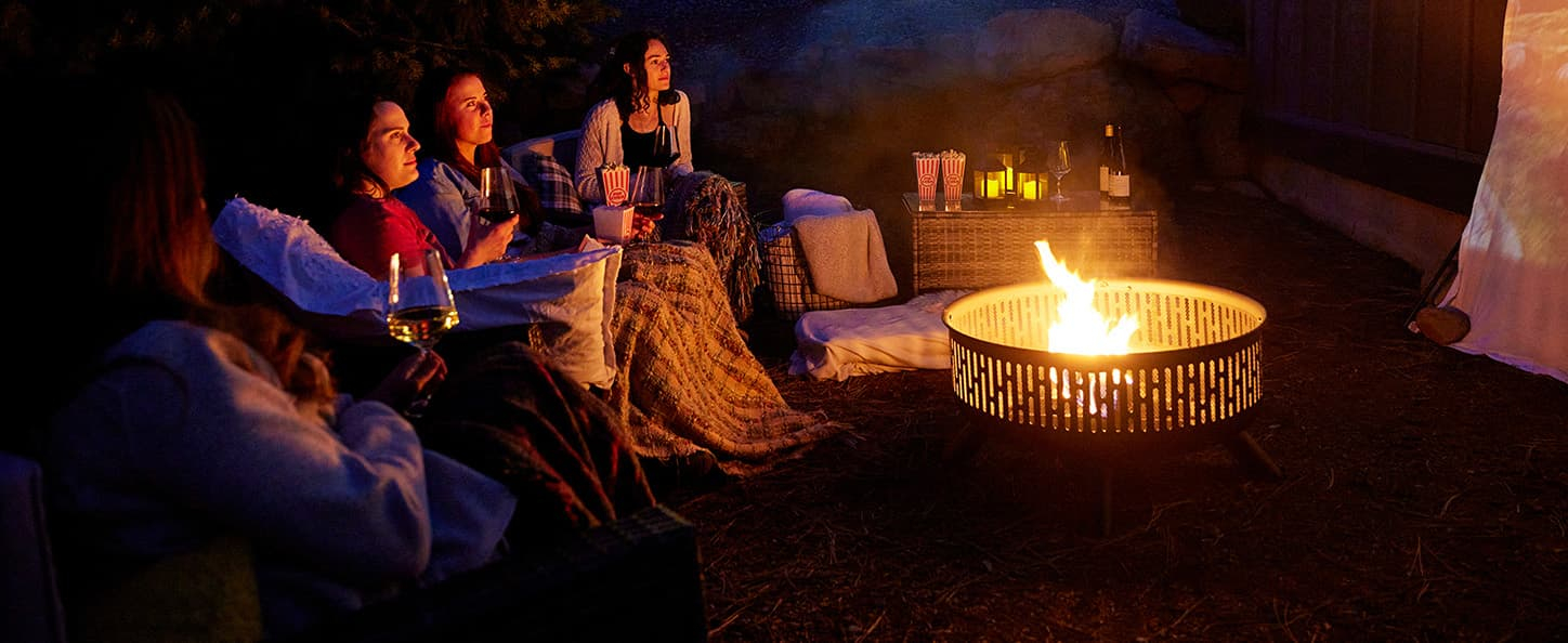 Group of ladies enjoying a fire in a fire pit while watching a movie outdoors
