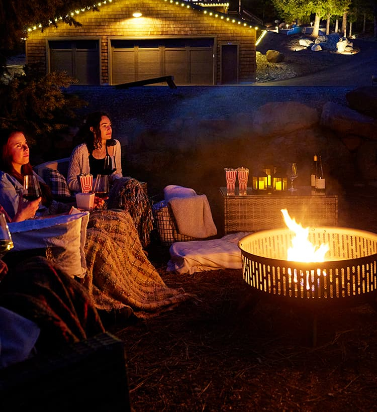 Group of ladies enjoying a fire in a fire pit while watching a movie outdoors