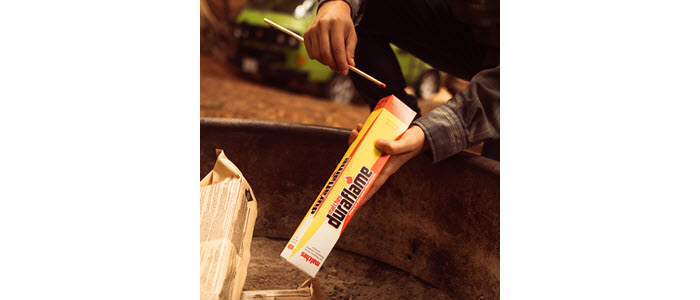 Person striking a DURAFLAME® SAFETY MATCH on box to light duraflame OUTDOOR firelogs in a firepit